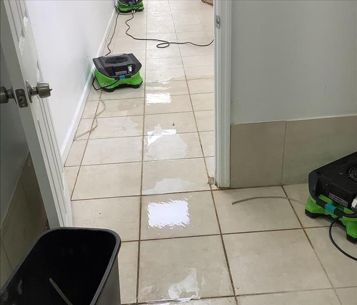 Water is on the floor of a hallway, drying equipment is setup to remove moisture from the air.